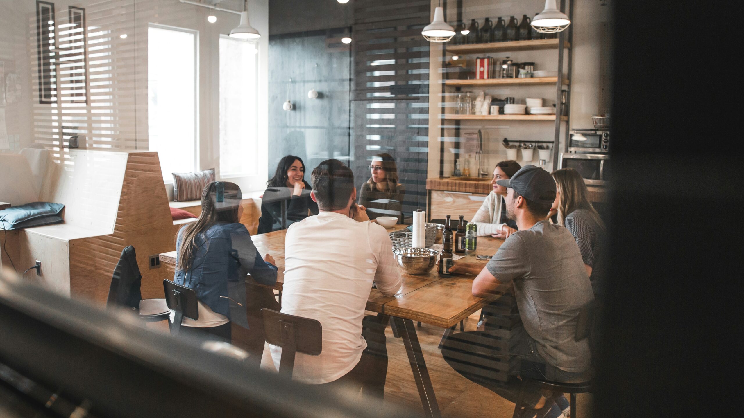 Group of People Sat Around a Table Talking and Drinking